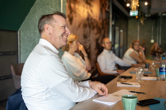 Man zittend aan tafel kijkt lachend toe.