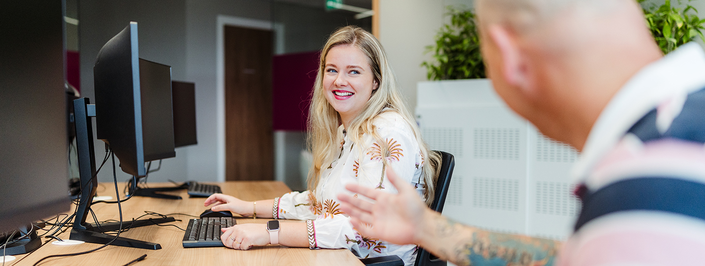 vrouw aan bureau kijkt lachend naar collega